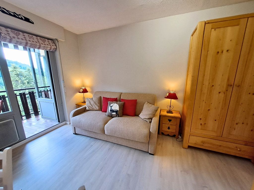 A room with a sofa, two bedside tables with lamps, a wooden wardrobe, and a sliding glass door leading to a balcony.
