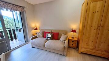 A room with a sofa, two bedside tables with lamps, a wooden wardrobe, and a sliding glass door leading to a balcony.