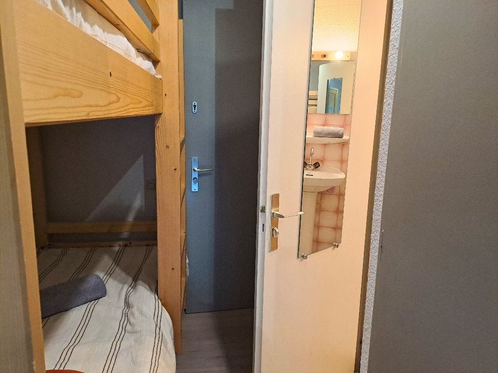A narrow hallway with a wooden bunk bed on the left and a bathroom with a mirror and sink on the right.