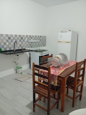 A compact kitchen with a gas stove, a refrigerator, and a dining table with chairs. - Cozy house in Ceará (Caponga)