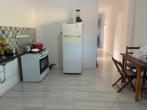 A compact kitchen with a stove, oven, and refrigerator, a dining table with chairs, and a tiled backsplash. - Cozy house in Ceará (Caponga)