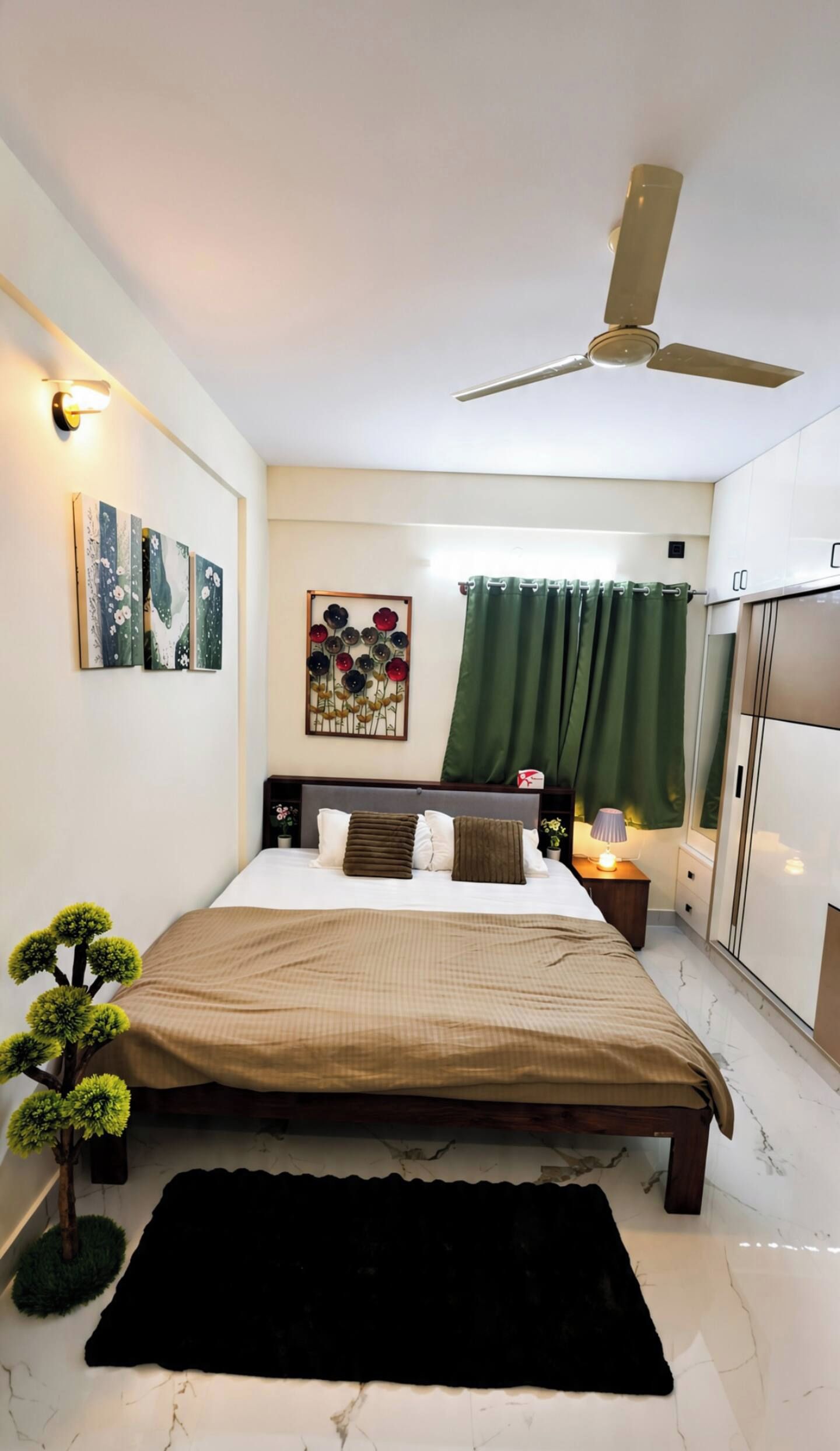 A bedroom with a bed, a ceiling fan, a nightstand, a lamp, a green curtain, and a wall-mounted artwork.