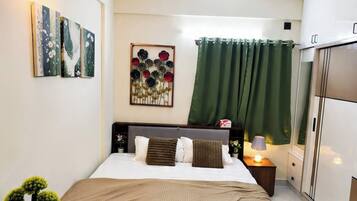 A bedroom with a bed, a ceiling fan, a nightstand, a lamp, a green curtain, and a wall-mounted artwork.