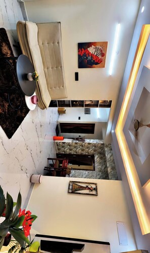 Un salon moderne avec un canapé, une table basse et un coin repas comprenant une table et des chaises. Un tableau est accroché au mur et une plante est posée sur le sol.