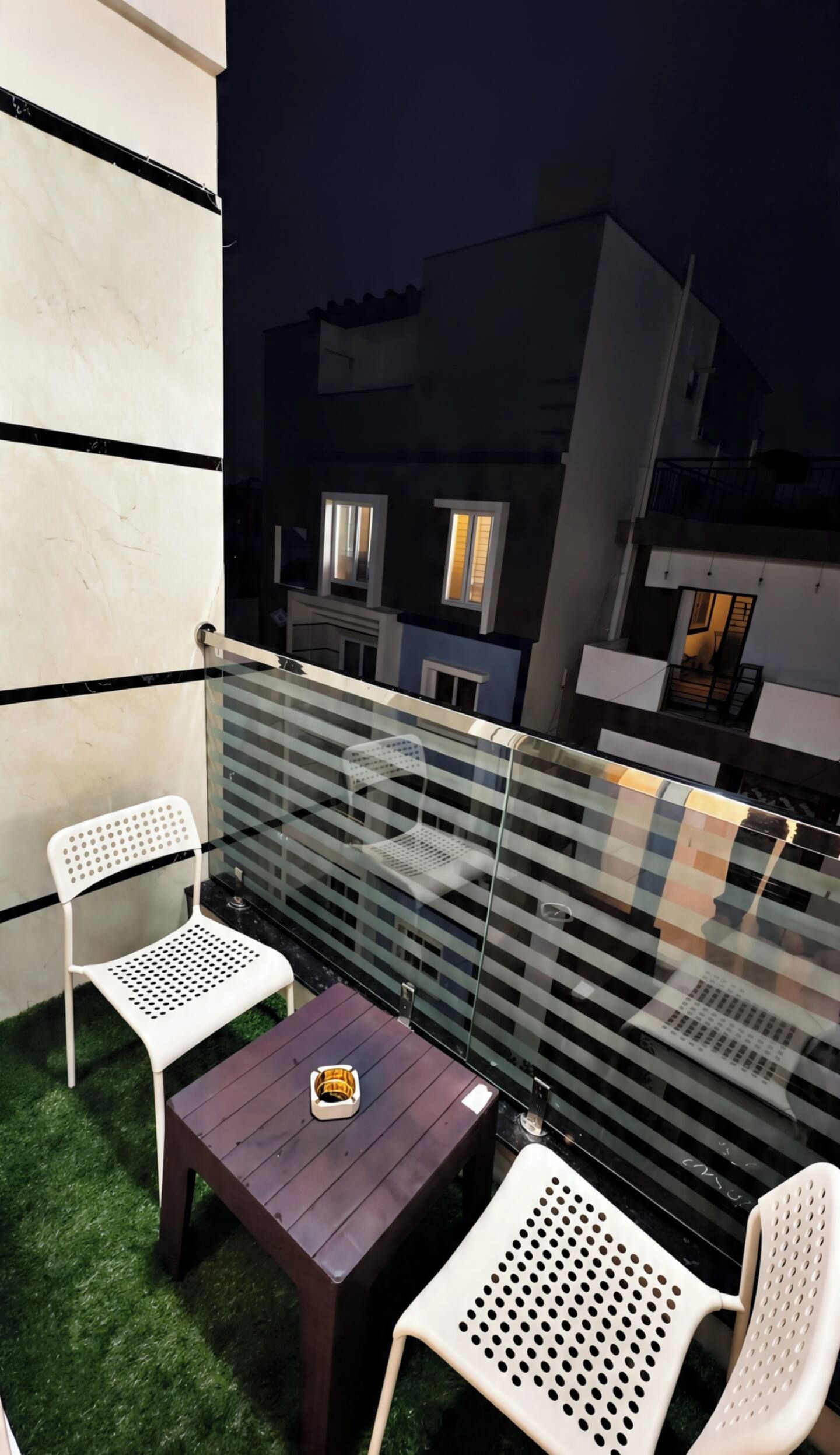 A balcony with two white chairs, a small table, and a glass railing.