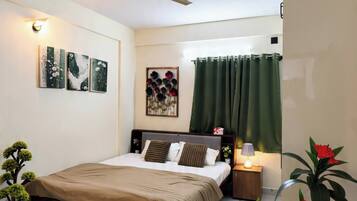 A bedroom with a bed, a ceiling fan, a nightstand, a lamp, and two potted plants.