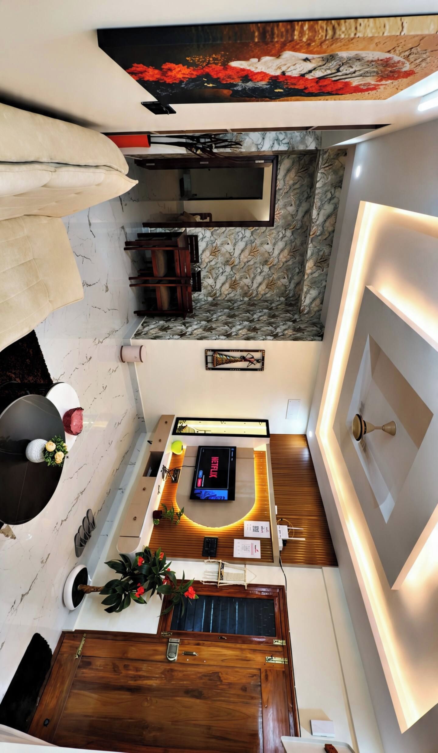 A modern living room with a flat-screen TV, wooden flooring, and a marble-patterned wall.