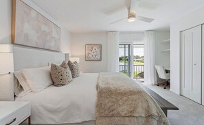 Quarto com cama, mesas de cabeceira, ventilador de teto, janela com cortinas e vista para o exterior.