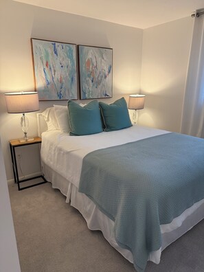 Ein Schlafzimmer mit einem Bett, zwei Nachttischen, zwei Lampen und abstrakter Wandkunst.