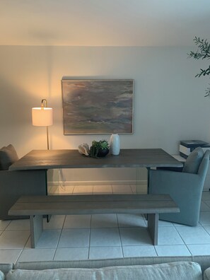 Ein modernes Wohnzimmer mit einer Couch, einer Bank, einem Tisch, einer Lampe, einem Gemälde und einer Pflanze.