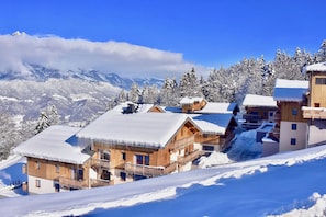 A snow-covered mountain lodge with wooden cabins, a ski lift, and a clear view of the surrounding mountains. - Ski aux pieds | Piscine Chauffée | Spa (Combloux)