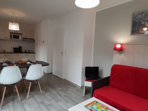 A compact living space with a dining area, a red sofa, and a television on a small table. - T2 au Pied des Pistes | Espace bien-être (Combloux)