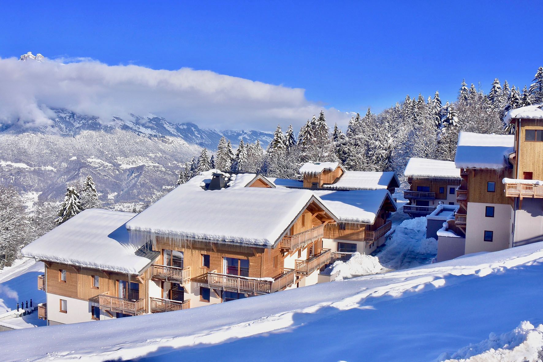 A snow-covered mountain lodge with wooden cabins, a ski lift, and a clear view of the surrounding mountains.
