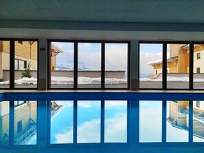 A hotel room with large windows overlooking a snowy landscape and a pool. - T2 au Pied des Pistes | Espace bien-être (Combloux)