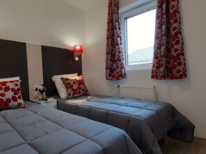 A bedroom with two beds, a nightstand, a lamp, and a window with curtains. - Directement sur les pistes | Piscine | Balcon (Combloux)