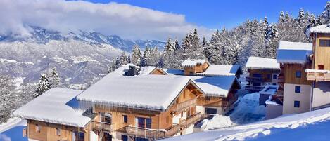 A snow-covered mountain lodge with wooden cabins, a ski lift, and a clear view of the surrounding mountains.