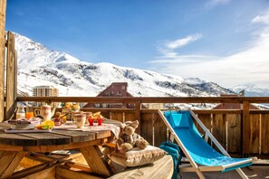 A wooden deck with a table set for breakfast, a slide, and a view of snow-covered mountains. - Ski aux Pieds | Piscine Chauffée | Balcon (Saint-François-Longchamp)
