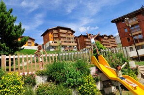 A playground with a yellow slide and a wooden fence. - Ski aux Pieds | Piscine Chauffée | Balcon (Saint-François-Longchamp)