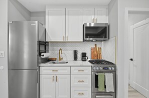 A modern kitchen with white cabinetry, stainless steel appliances, a herringbone-patterned backsplash, and a gas stove. - Sandbox and Sunshine 8 (Margate City)