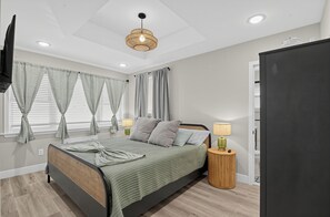 A bedroom with a bed, bedside lamps, a television, and a wardrobe. - Sandbox and Sunshine 8 (Margate City)