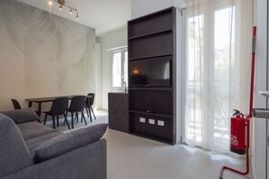 A modern living room with a sofa, a dining table with chairs, a flat-screen TV mounted on a wall, and a fire extinguisher. - Newly renovated apartment with a balcony, a 10-minute walk to Bocconi, sleeps 4 (Milan)