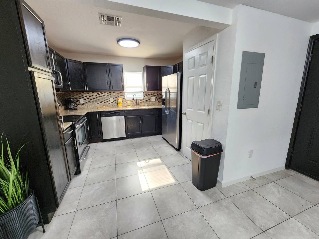 A modern kitchen with dark cabinets, a stainless steel refrigerator, and a tiled floor.