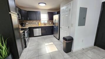 A modern kitchen with dark cabinets, a stainless steel refrigerator, and a tiled floor.