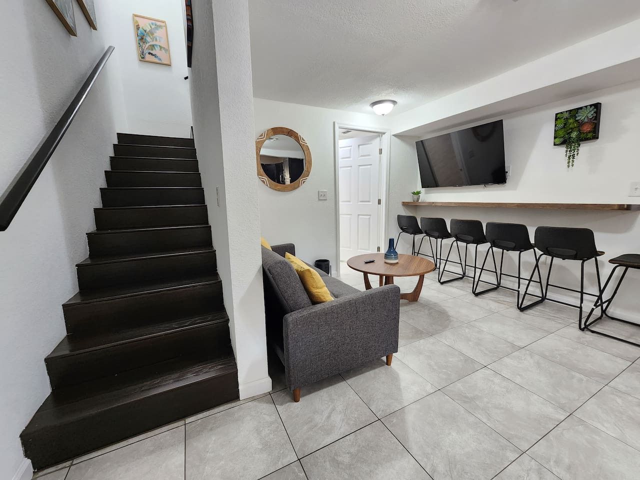 Una escalera que conduce a una sala de estar con un sofá, una mesa redonda y un televisor.