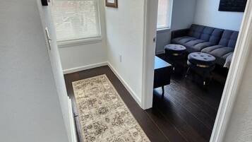 A hallway leading to a living area with a dark wood floor, a patterned rug, and a dark-colored sofa with matching stools.