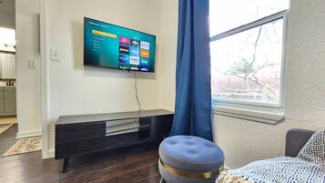 A modern living room with a flat-screen TV mounted on the wall, a dark wooden entertainment unit, a blue curtain, and a patterned throw on a couch.