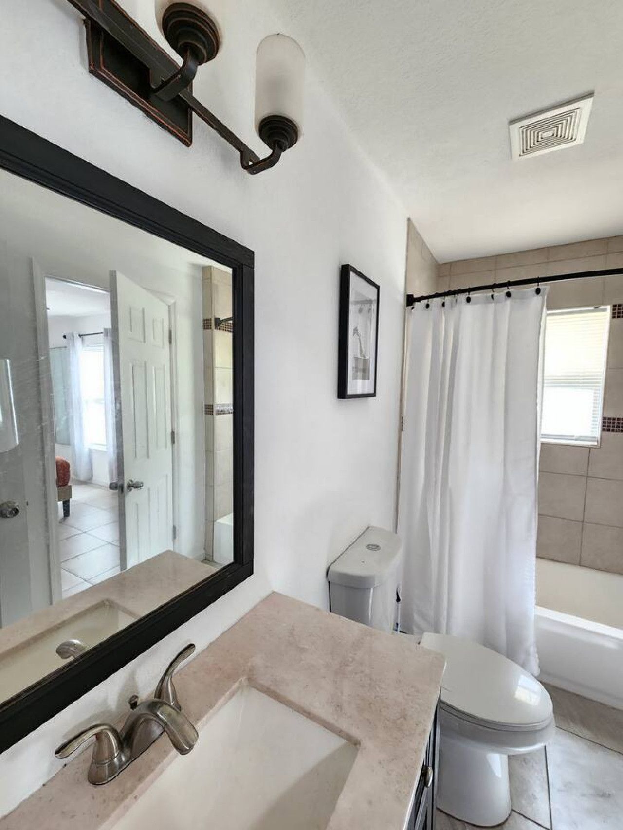Ein Badezimmer mit Waschbecken, Spiegel, Toilette, Duschvorhang und einem gerahmten Bild an der Wand.