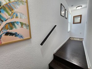 Ein Flur mit einer strukturierten weißen Wand, einem gerahmten abstrakten Gemälde, einer schwarzen Handläufe und einem dunklen Holzboden.