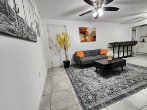 Ein Wohnzimmer mit grauem Sofa, Couchtisch, Deckenventilator und Teppich mit Muster.