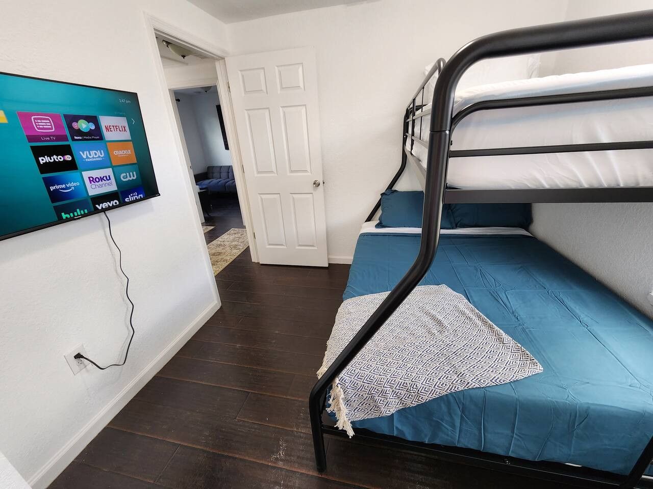 A room with a bunk bed, a television displaying streaming services, and a door leading to another room.