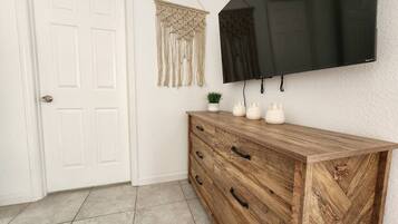 A room with a wooden herringbone-patterned dresser, a flat-screen TV mounted on the wall, and a macramé wall hanging.