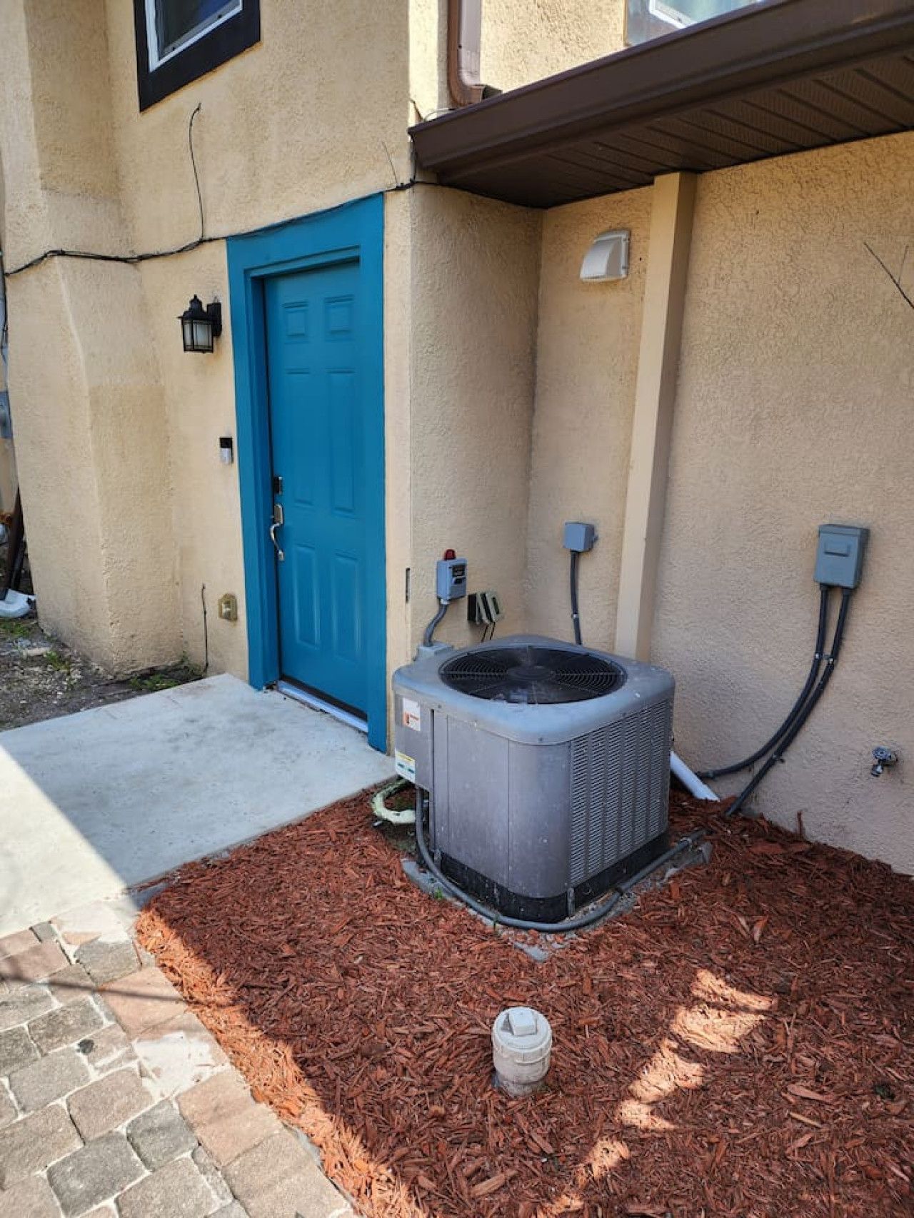 An outdoor air conditioning unit, a blue door, and a small white object on the ground.