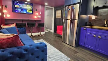 Un saló modern amb un sofà blau, una televisió de pantalla plana i una zona de cuina amb armaris morados.
