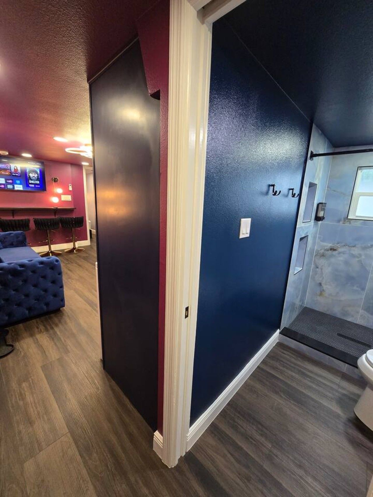 A room with a dark blue accent wall, a wooden floor, a tufted blue sofa, and a television mounted on the wall.