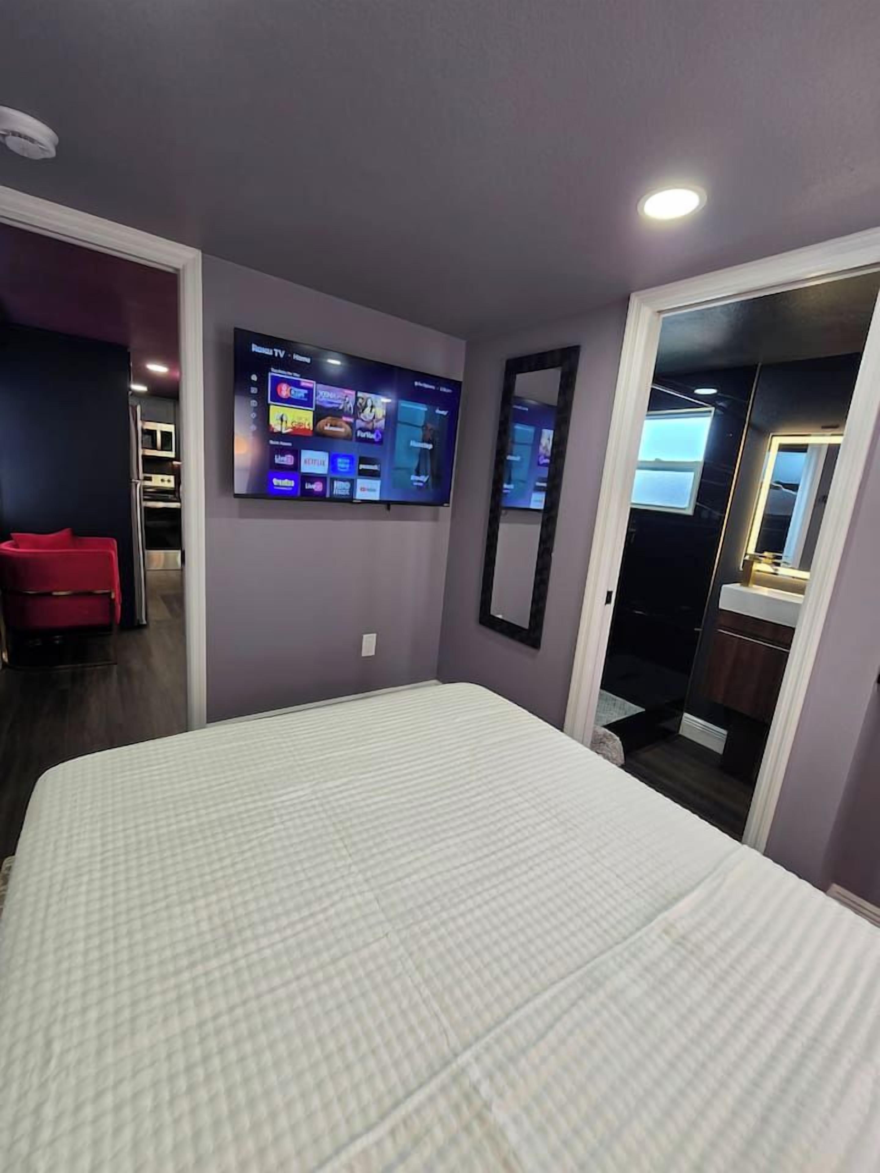 Une chambre d’hôtel avec un lit, un téléviseur fixé au mur, un miroir et une porte donnant sur une salle de bain.