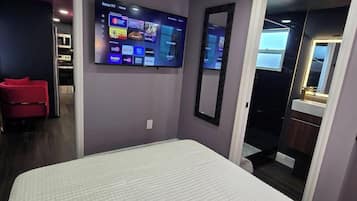 Une chambre d’hôtel avec un lit, un téléviseur fixé au mur, un miroir et une porte donnant sur une salle de bain.