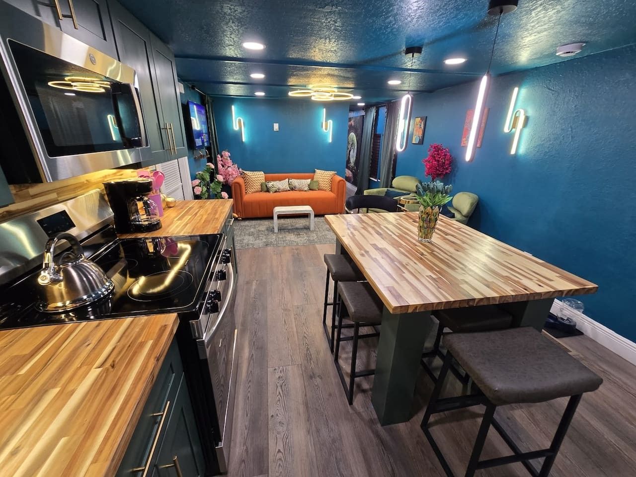 A modern kitchen with a wooden countertop, stainless steel appliances, and a dining area with a wooden table and bar stools.