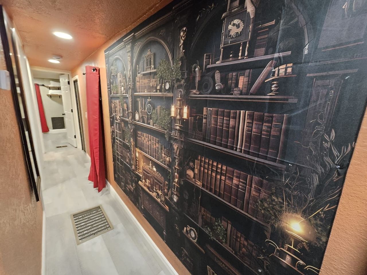 Un couloir orné d’une fresque représentant des étagères à livres et surmonté d’un rideau rouge.