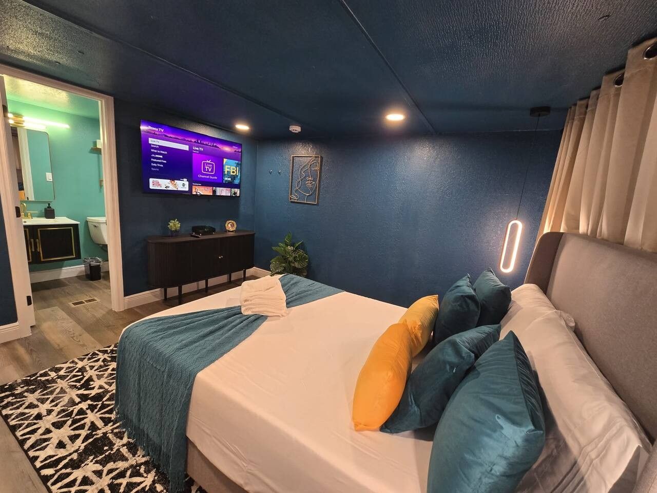 Une chambre d’hôtel avec un lit, un téléviseur fixé au mur, un bureau et une salle de bain visible à travers une porte ouverte.