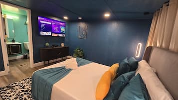 Une chambre d’hôtel avec un lit, un téléviseur fixé au mur, un bureau et une salle de bain visible à travers une porte ouverte.