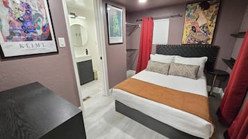 A bedroom with a bed, a bedside table, a red curtain, and artwork on the walls.