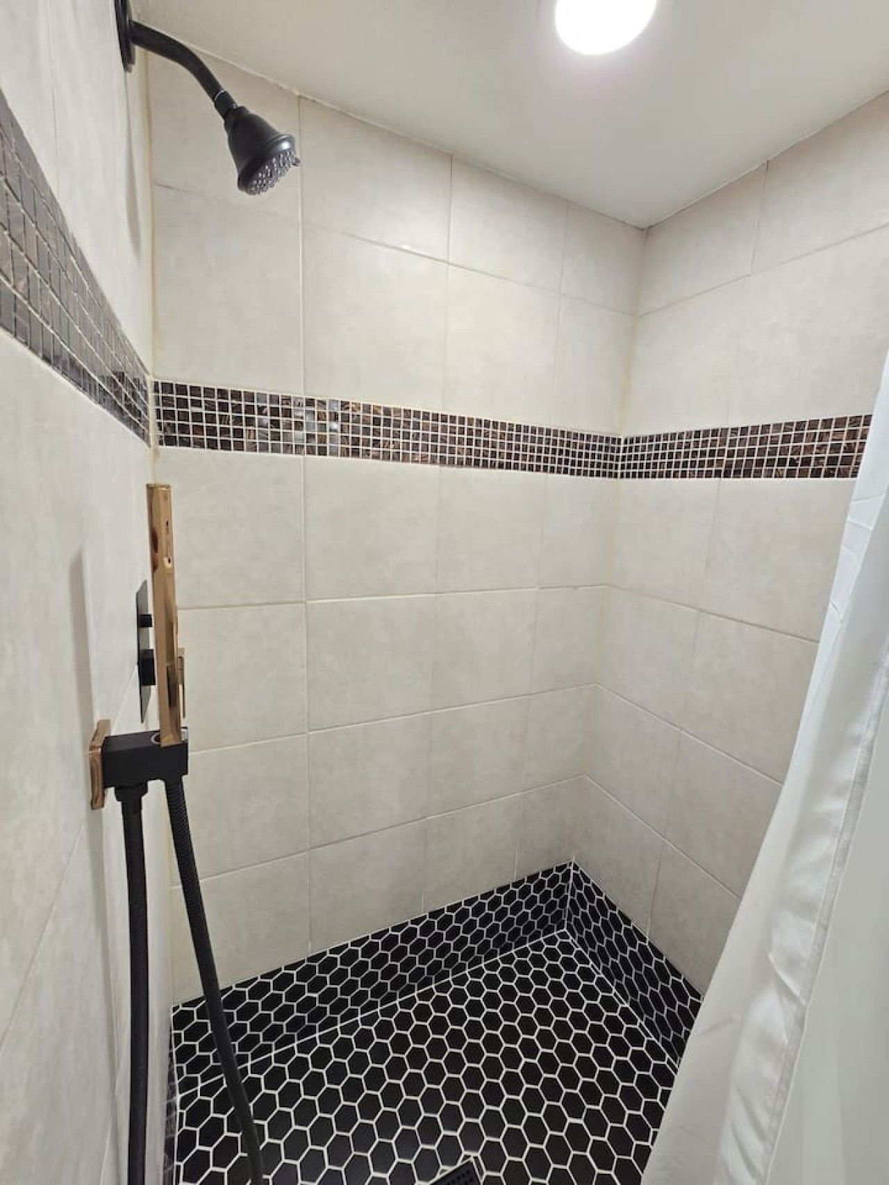 A shower area with a tiled floor, a showerhead, and a wall-mounted light fixture.