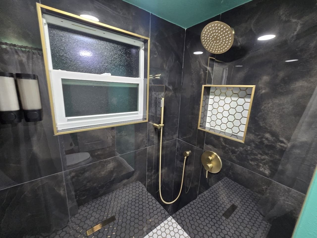 Een moderne badkamer met een douchecabine van glas, een raam en een decoratieve zeshoekige spiegel.