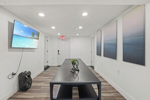 Ein Konferenzraum mit einem langen Tisch, einem Fernseher an der Wand und einer Tür mit einem Ausgangsschild.
