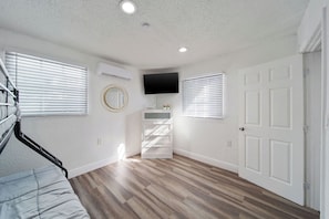 A room with a wooden floor, white walls, a flat-screen TV mounted above a white cabinet, and a door on the right. - 3-bedroom apartment with AC near Brickell/Downtown (Miami)