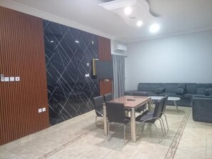 Un saló modern amb un sofà, una taula de dinar amb cadires i un televisor fixat a la paret.